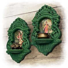 two green ornate wall hangings with pictures on them and a gold vase in the middle