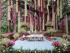 an outdoor wedding setup with pink and white flowers hanging from the ceiling, surrounded by greenery