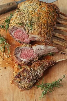 a large piece of meat on a wooden cutting board next to a knife and sprig of rosemary