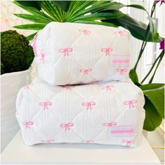 two white blankets with pink bows are stacked on top of each other in front of a potted plant