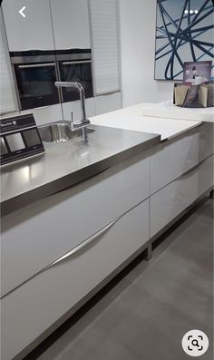 a kitchen with white cabinets and stainless steel counter tops, along with a large painting on the wall