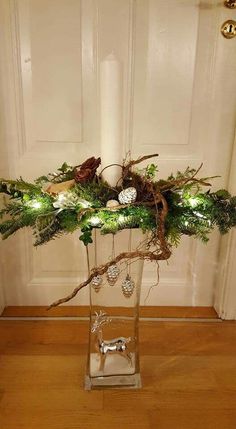 a glass vase filled with greenery and ornaments on top of a wooden floor next to a door