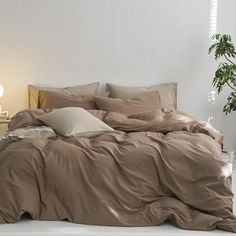 an unmade bed in a white room with a potted plant next to it