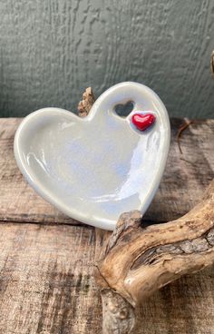 a white heart shaped dish with a red nose on it sitting on top of a piece of drift wood