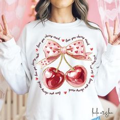 a woman wearing a white sweatshirt with two cherries on the front and one heart on the back