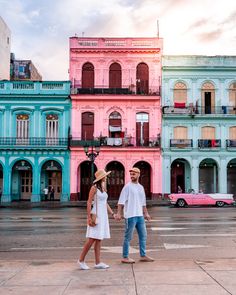 a man and woman holding hands while standing in front of colorful buildings on the street