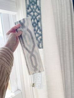 a person is holding up a piece of fabric next to a window with white curtains