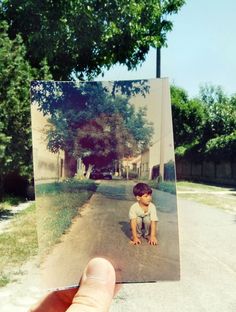 a hand holding up a polaroid photo of a boy sitting on the side of a road