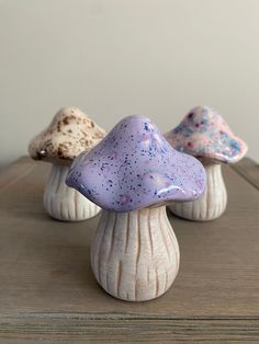 three small ceramic mushrooms sitting on top of a wooden table next to each other in different colors