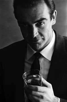 a man wearing a suit and tie holding a glass in his hand with the words booze like bond on it