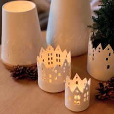 three lit candles sitting on top of a table next to pine cones and white vases