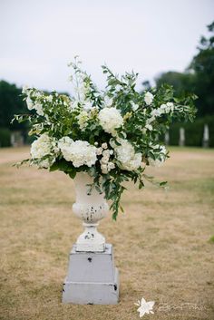 a vase with white flowers in it sitting on the ground next to a grass field