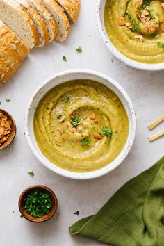 two bowls filled with green soup next to sliced bread