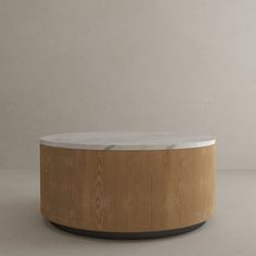 a round wooden table sitting on top of a white floor next to a gray wall