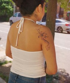 a woman with a tattoo on her back standing in front of a tree and street