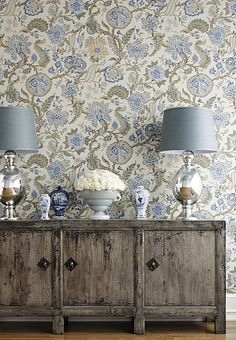 two lamps on top of a dresser next to a wall with blue and white flowers