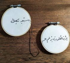 two embroidered hoops with writing on them sitting on a wooden table next to each other