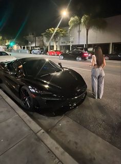 a woman standing next to a black sports car