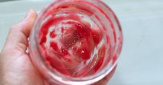 a hand holding a glass filled with red liquid and strawberries on top of it