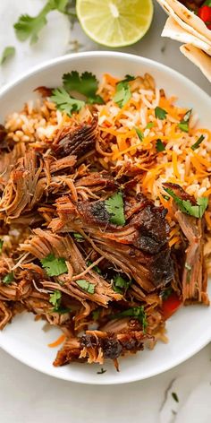 shredded beef and rice on a white plate with lime wedges next to the plate