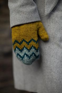 a person wearing a gray coat and yellow mittens with blue zigzag on it