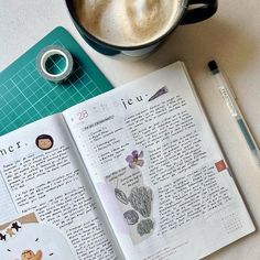 an open book sitting on top of a table next to a cup of coffee and pen