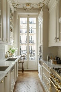 a narrow kitchen with white cabinets and gold trim on the ceiling, along with marble counter tops