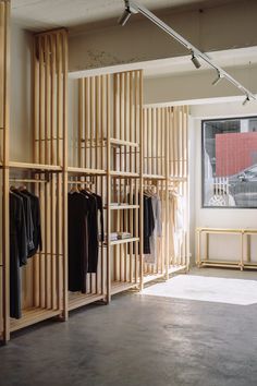 an empty room with wooden shelves and clothes on hangers in front of a window