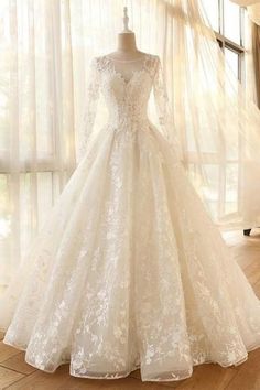 a white wedding dress on display in front of a window with sheer drapes and curtains