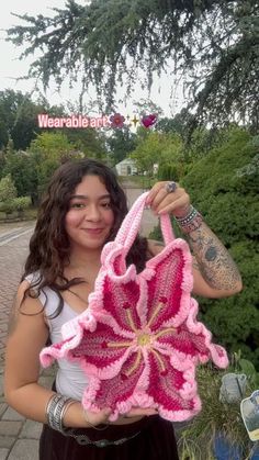 a woman holding up a pink crocheted flower