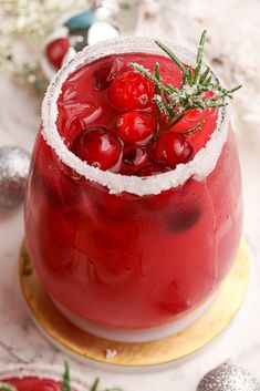 a red drink in a glass with ice and garnish on the rim, surrounded by christmas decorations