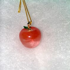 a red apple hanging from a gold chain on a white surface with tiny drops of water