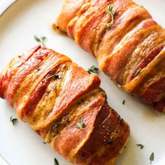 two pieces of meat wrapped in bacon sitting on a white plate with green garnish