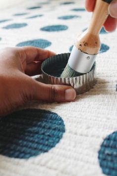 someone is using a brush to paint the inside of a cupcake tin on a polka dot tablecloth