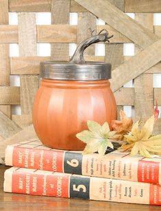 two books are stacked on top of each other next to a pumpkin jar and some leaves