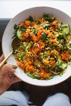 a person holding a white bowl filled with rice and veggies, topped with chopsticks