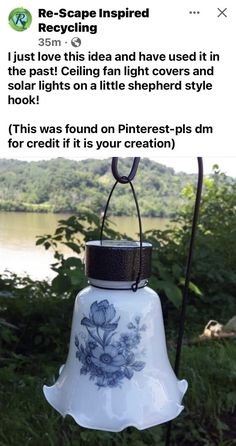 a bell that is hanging from a pole in the grass next to some trees and water