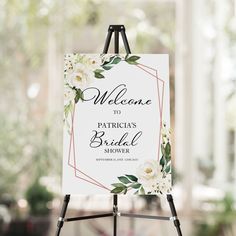 a welcome sign with white flowers is on an easel in front of a window