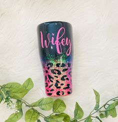 a pink and black tumbler with the word wife on it next to some leaves