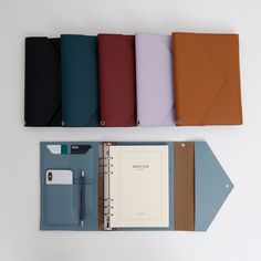 five notebooks lined up next to each other on a white surface with one opened and the other closed