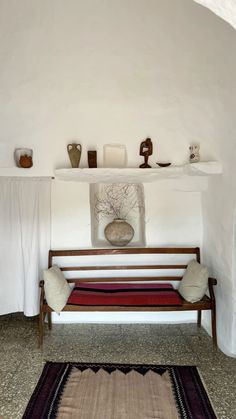 a white room with a bench, rug and vases on the wall next to it