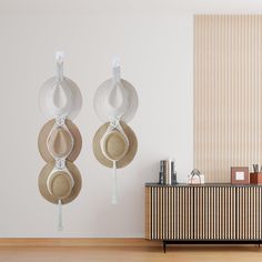 three hats hanging on hooks in front of a white wall with vertical blinds and wooden flooring