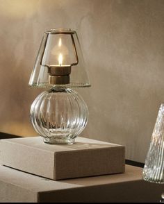 a clear glass table lamp sitting on top of a box next to a small candle