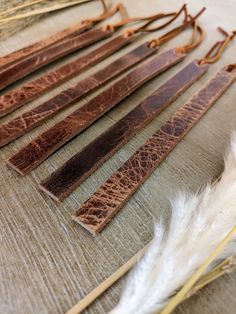 several pieces of leather sitting on top of a wooden table next to some white feathers