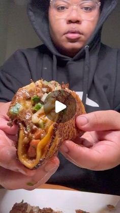 a man in a hoodie is holding a sandwich with meat and vegetables on it