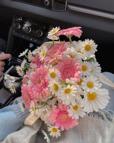 a bouquet of pink and white daisies in someone's lap with the steering wheel behind them