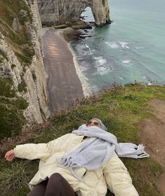 a woman laying on the ground next to an ocean and cliff area with cliffs in the background