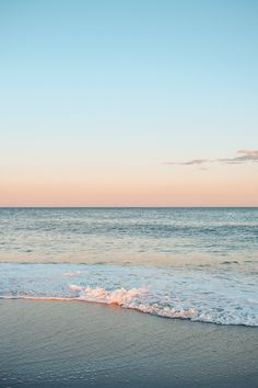 an ocean view with waves coming in to shore and the sun setting on the horizon