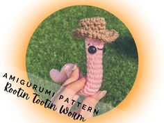 a hand holding a knitted toy in the shape of a worm wearing a straw hat