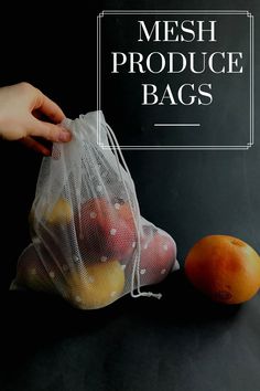 mesh produce bag with oranges and apples in it on a black surface next to a person's hand